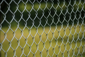 Fototapeta premium Close-up of metal chain link fence with blurred green background.