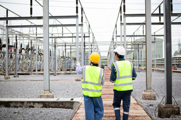 Two engineers are working at high voltage substation wearing safety helmets and reflective vests...