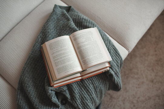 Open paper books with knitted textile on white velveteen couch in living room at home in dark. Coziness.