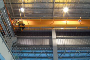 Overhead crane in factory or warehouse building. Industrial machine or lifting equipment with hoist, hook and wire rope move on beam structure for process in storage, manufacturing and production.