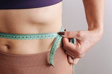 Slim woman measuring waist. Body with measuring tape. Fitness and weight loss concept. Healthy lifestyle and diet progress. Closeup torso in activewear. Fit female checking size.