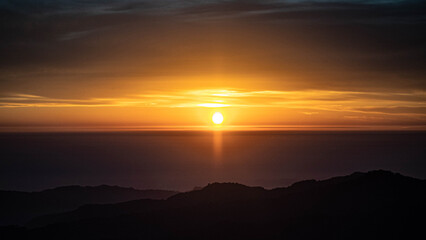 Sunrise over the calm horizon with layered mountain silhouettes under golden sky tones