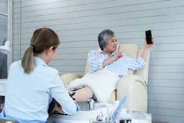 Happy senior woman smiling posing with smartphone during cozy foot spa session receiving treatment from spa professional promoting beauty relaxation wellness lifestyle personal grooming health care