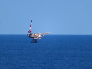 A lone offshore oil platform stands majestically in the vast, deep blue ocean under a clear, serene sky. The platform, a symbol of industry, contrasts sharply with the untouched beauty of nature.