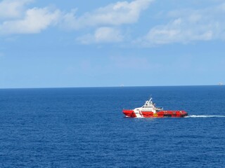 Red and white supply vessel navigates the deep blue ocean under a partly cloudy sky. A tranquil scene of maritime transport at sea.