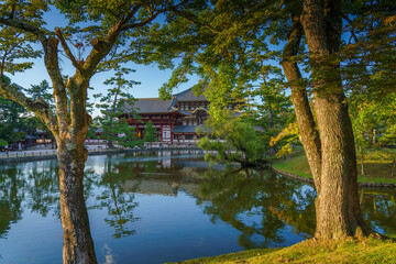 Nara, Japan - Sep 26 2024, Panoramic view across the pond and trees to the facade of Todaiji Temple, Great Buddha Hall, with a blue cloudy sky, Nara, Japan