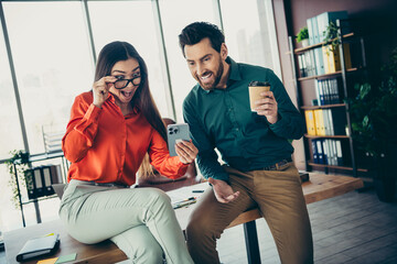 Two professional colleagues excitedly view a phone screen as they collaborate in a brightly lit...