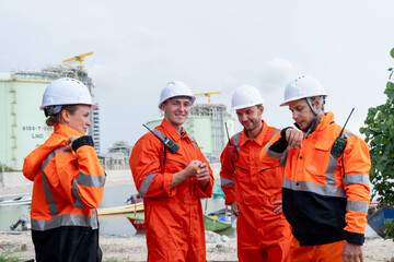 Workers in safety gear collaborating near industrial site with boats in background during daytime