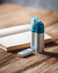 Multi-dose inhaler and digital medication counter placed on a wooden table beside an open patient journal in soft daylight, symbolizing personal respiratory care — ai generative.