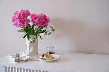 A charmingly decorated table that showcases fresh peonies flowers, an elegant plate with cheesecake, and a wonderfully serene atmosphere