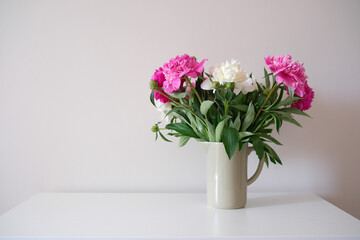 A beautifully charming arrangement of pink and white peonies in a simple vase on white vase.