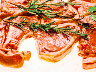 Premium quality marinated lamb loin chops and rosemary herb on white background. Uncooked raw meat...