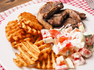 Dinner meal with cooked lamb loin chops, potato lattice and fresh salad with sour cream. Close up. Fine tasty dinner.