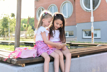 Two young girls sitting outdoors using smartphones