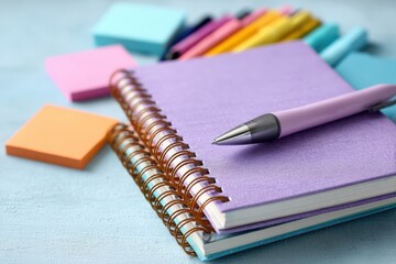 Close up of spiral notebooks with colorful sticky notes and pens on a light blue desk, creating a stationery setup for study or planning, ready for a creative work.