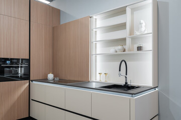 modern built-in kitchen in light color with upper and lower cabinets. glass doors, steel faucet and sink, built-in kitchen appliances. wine glasses on shelves. kitchen unit