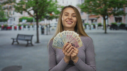 Woman smiling and holding polish zloty banknotes on a city street, showcasing wealth against an...