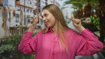 Woman in pink shirt joyfully dancing on a city street lined with palm trees, expressing happiness...