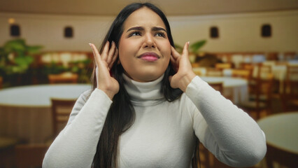 Woman with ears covering gesture in restaurant captures young latin hispanic indoor coffee scene...