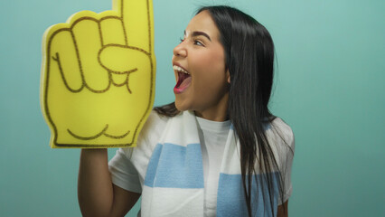 Woman enthusiastically cheering with a large foam finger in front of an isolated green background,...