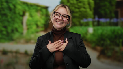 Woman smiling in outdoor park setting with greenery background wearing glasses and black jacket showcasing positivity and relaxation in a natural environment