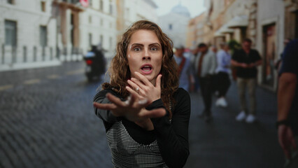 Obraz premium Woman shielding face in fear on bustling city street with blurred pedestrians and motorbike in background.