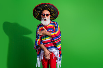 Fototapeta premium Charismatic elderly man wearing colorful poncho and sombrero striking a funny pose against vibrant green background