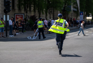 Law enforcement officer in fluorescent safety vest running urgently on city street during daytime...