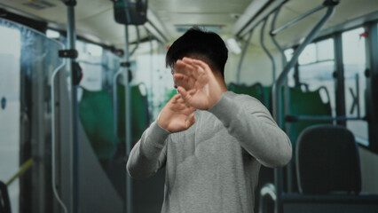 Young man in a bus wearing a gray sweater looks annoyed with an indoor background and blurry green...