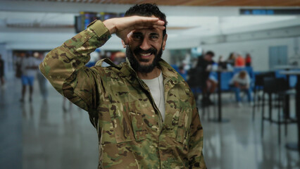Hispanic man in military uniform saluting in a bustling airport terminal capturing a moment of...