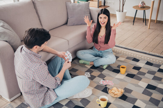 Young couple enjoying quality time together playing cards indoors during a sunny day in a cozy apartment space with snacks and beverages