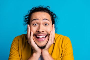 Happy young man with curly hair expressing excitement against a bright blue background wearing a...