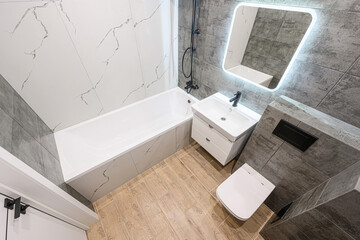 modern bathroom featuring a white bathtub, white sink with drawers, toilet, an illuminated mirror, and a contrasting tile design of white and gray