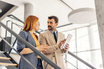 Serious businesspeople descending stairs with tablet in hands and discussing project.