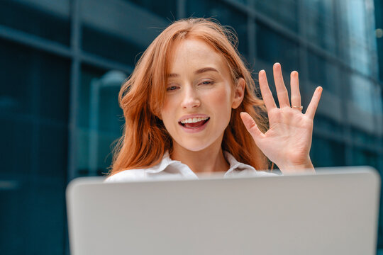 Young woman waves while video chatting outdoors in a modern urban setting during daylight