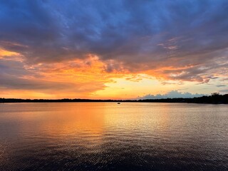 Stunning sunset over a calm lake with dramatic clouds and vibrant reflections on the water. A peaceful and colorful nature scene perfect for backgrounds or relaxation themes.