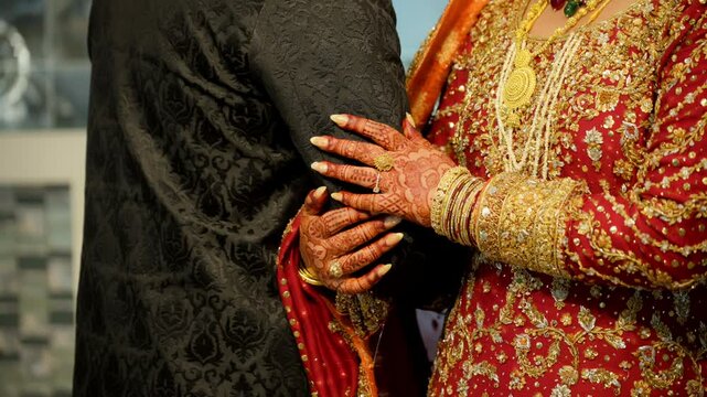 Wedding couple hands while holding each other, dressed in the traditional red and black Asian clothes, Elements of hindu wedding. Close up