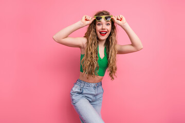 Young fashionable woman in green top and jeans posing against pink background, expressing happiness...