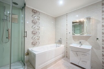 Bright bathroom featuring a bathtub, glass shower, vanity with a sink, and beige-toned tile walls with floral accents