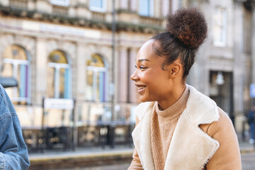 Fototapeta premium Young woman smiling while enjoying conversation outdoors in city street during a sunny day