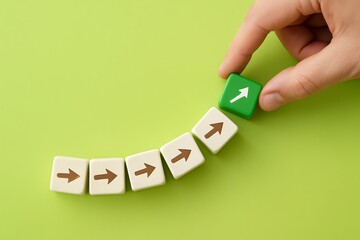 Hand Placing Green Block with Upward Arrow Among Beige Blocks on Green Background Symbolizing Change, New Direction, Innovation, and Progress in Business Strategy and Sustainable Development Concepts.