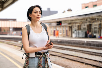 Woman waiting at railway station with smartphone during cloudy day in urban environment