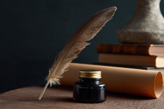 Classic feather quill, ink pot and parchment scroll on antique desk surrounded by old books