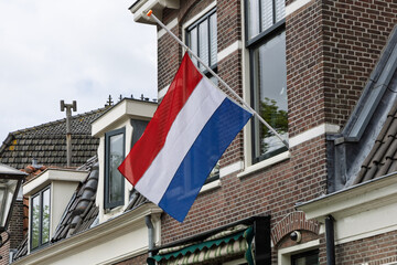 The Dutch flag flies at half-mast from a traditional brick building, signifying mourning or remembrance in the Netherlands.