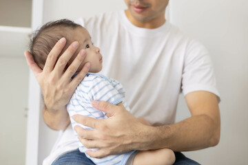 A man is holding a baby in his arms. The baby is wearing a blue and white striped shirt. The man is smiling at the baby, and the baby is looking up at him
