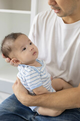 A man is holding a baby in his arms. The baby is wearing a blue and white striped shirt. The man is smiling at the baby, and the baby is looking up at him
