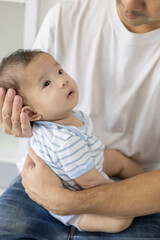 A man is holding a baby in his arms. The baby is wearing a blue and white striped shirt. The man is smiling at the baby, and the baby is looking up at him
