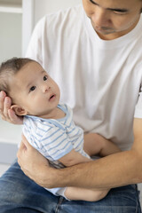 A man is holding a baby in his arms. The baby is wearing a blue and white striped shirt. The man is smiling at the baby, and the baby is looking up at him
