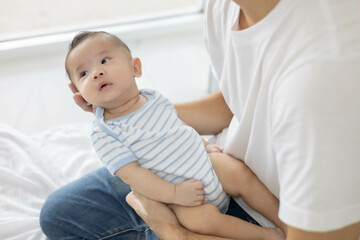 A man is holding a baby in his arms. The baby is wearing a blue and white striped shirt. The man is smiling at the baby, and the baby is looking up at him
