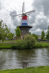 Classic Dutch windmill, Molen de Valk in Leiden, stands tall by a tranquil canal under a dramatic sky. A timeless symbol of Dutch heritage and scenic beauty.